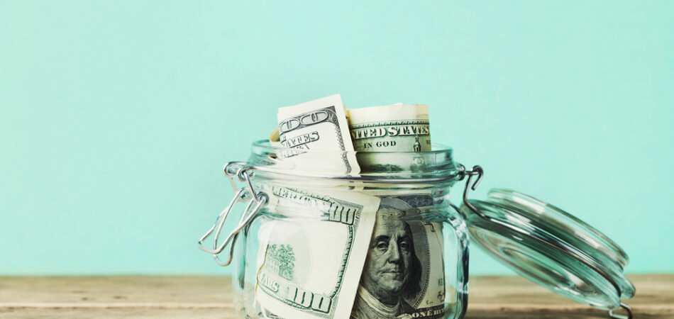 Dollar,bills,in,glass,jar,on,wooden,table.,saving,money